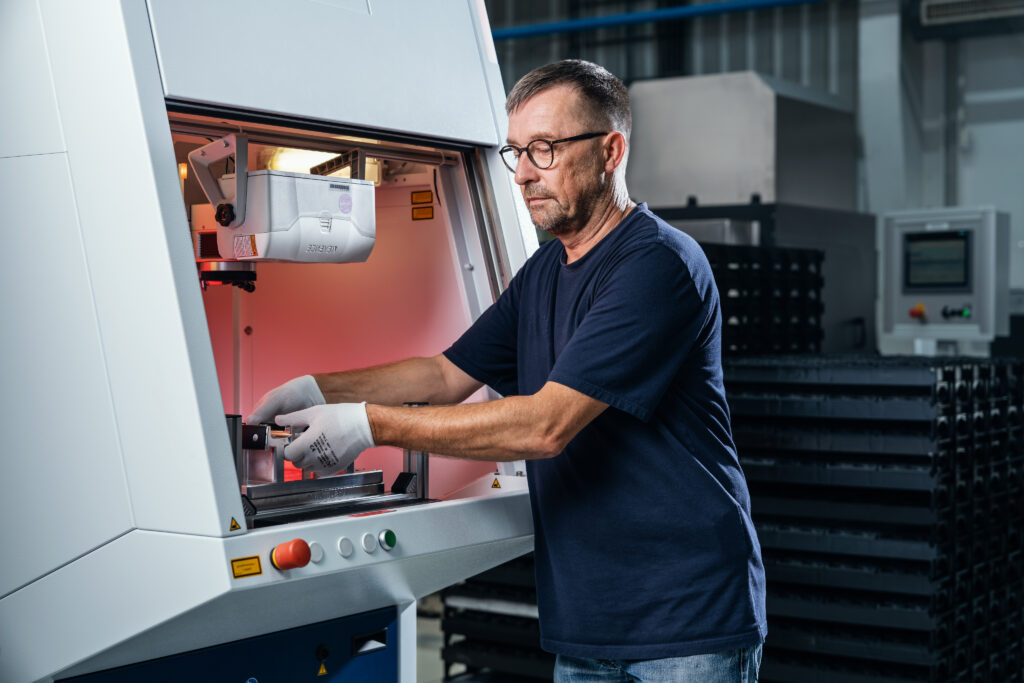Mann mit Handschuhen bedient eine industrielle Maschine in einer Werkhalle.